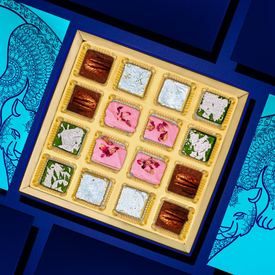 
                      
                        Assorted Indian burfi sweets in a decorative box, featuring pistachio, kaju, pecan, and rose coconut varieties, surrounded by ornate blue and teal patterns
                      
                    