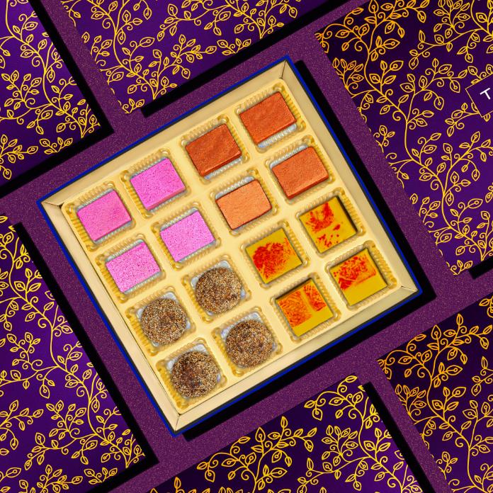 
                      
                        Colorful vegan mithai collection in elegant purple and gold packaging, featuring 16 pieces of assorted Indian sweets in vibrant hues of pink, orange, yellow, and brown, arranged in a decorative box
                      
                    