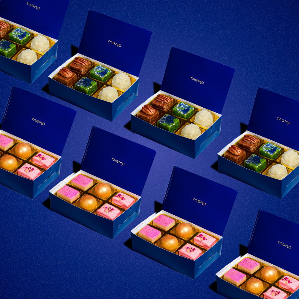 Assorted colorful Indian sweets in elegant blue TAGMO gift boxes, arranged neatly on a deep blue background. Each box showcases six pieces of vibrant mithai, including kaju katli, ladoos, and burfis, perfect for party favors or gifting.