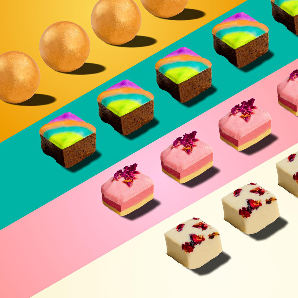 
                      
                        Colorful assortment of Indian sweets including golden spheres, square green treats, pink rectangular desserts, and white cubes with red garnish, arranged in neat rows on vibrant yellow, teal, pink, and white backgrounds.
                      
                    