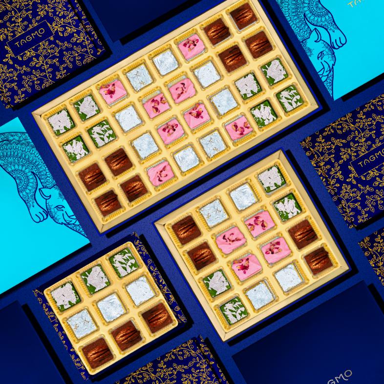 
                      
                        Assorted Indian burfi sweets in elegant gift boxes, showcasing various flavors like pistachio, kaju, and rose coconut, presented against a vibrant blue background with decorative packaging designs.
                      
                    