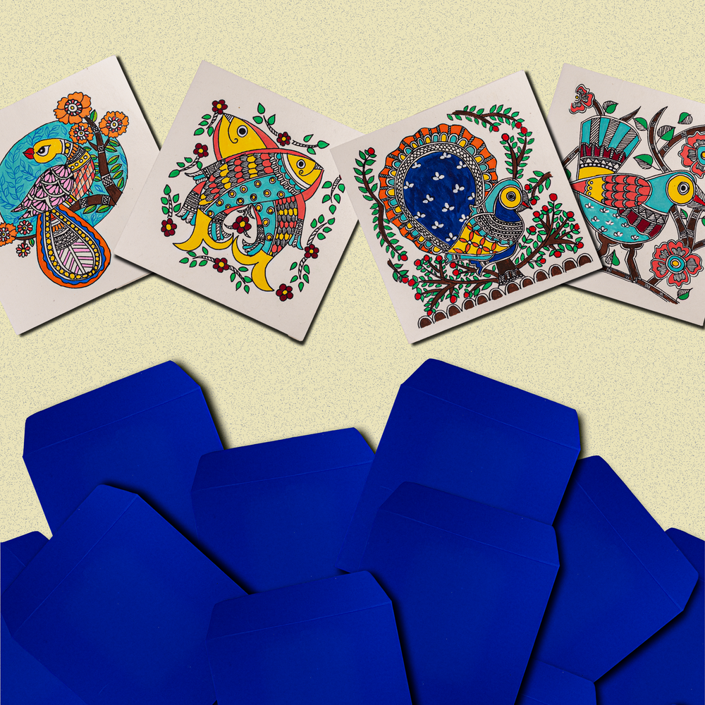 Colorful hand-painted greeting cards featuring Madhubani-inspired folk art designs of fish, peacocks, and other animals, displayed above a group of vibrant blue envelopes on a textured background.