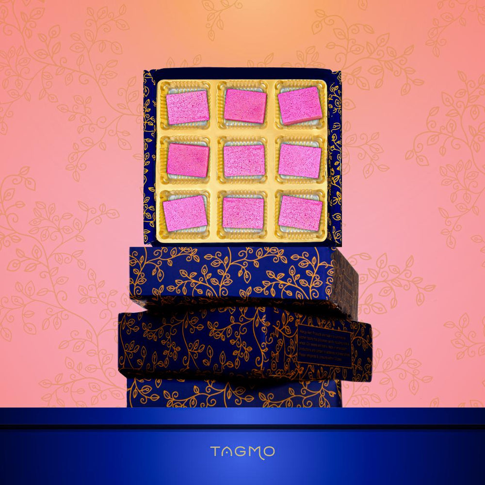 Elegant Kaju Katli box featuring nine pink diamond-shaped sweets arranged in a decorative navy and gold floral patterned container, showcasing TAGMO's unique twist on the classic Indian dessert with a vibrant pink dusting instead of traditional silver leaf