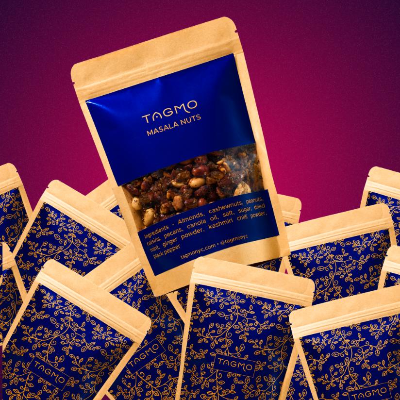 
                      
                        Colorful display of Tagmo's Masala Nuts packages, featuring a large gold and blue bag showcasing the mixed nuts blend, surrounded by smaller blue and gold patterned bags, arranged on a vibrant purple background.
                      
                    