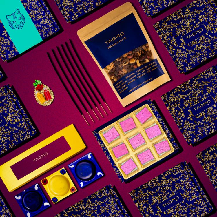 
                      
                        Colorful Diwali gift box featuring assorted traditional items including katli sweets, masala nuts, diyas, incense sticks, and decorative packaging on a vibrant maroon background with blue and gold patterns
                      
                    