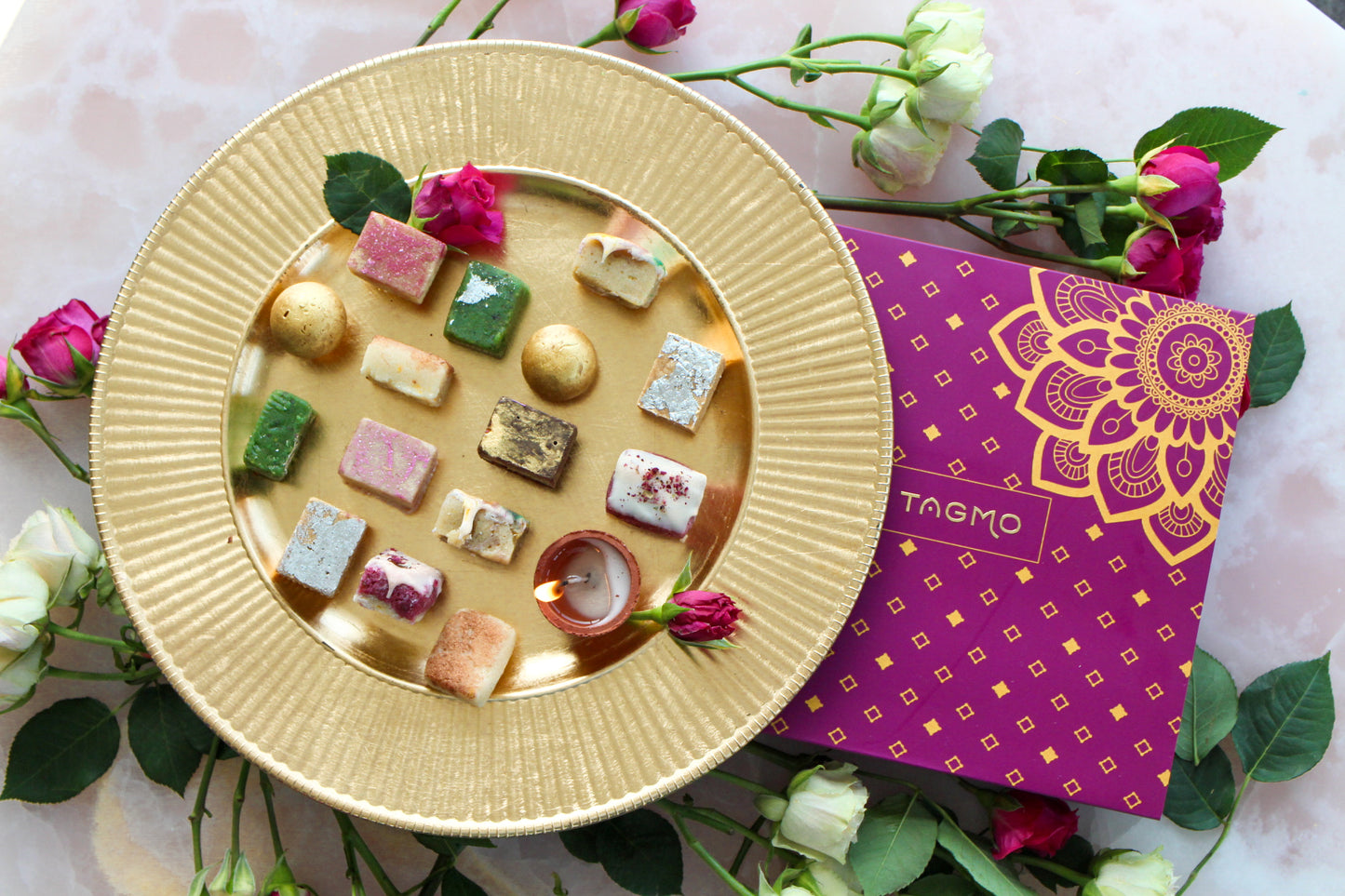 A colorful assortment of traditional Indian sweets, or mithai, arranged in an elegant gold dish, alongside a vibrant purple and gold box, creating a visually appealing and enticing display for the "Build Your Own Mithai Box" Shopify product.