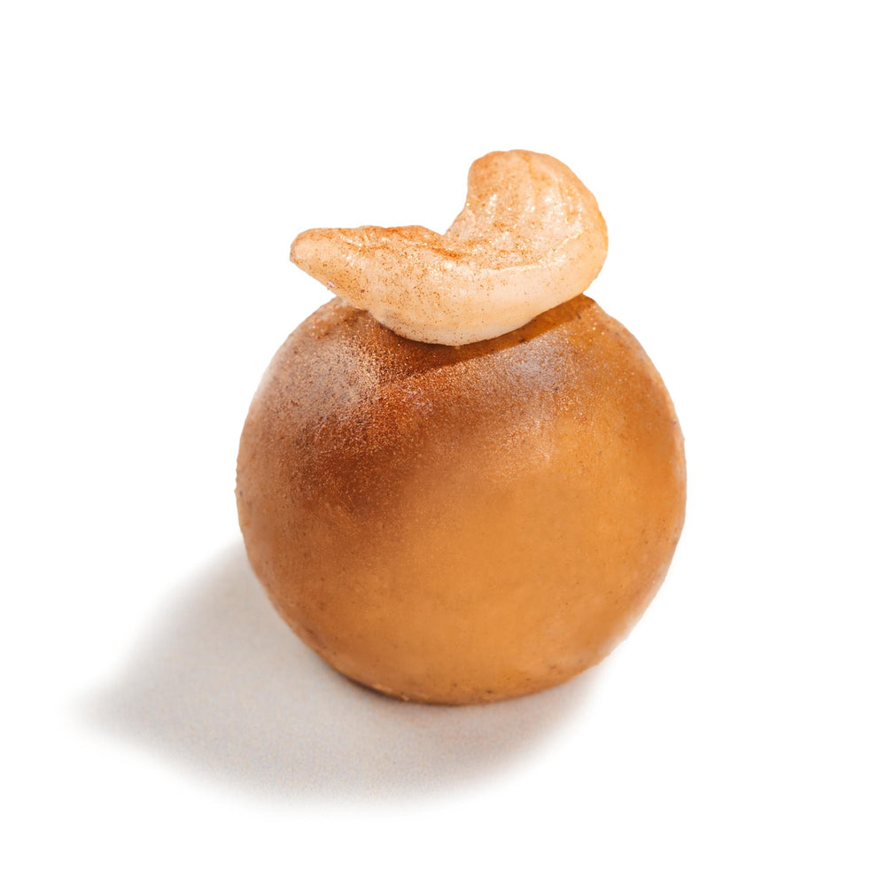 Golden spherical Panjeri ladoo with a curved cashew nut on top, showcasing the traditional Indian sweet from Nani ke Ladoo box by TAGMO, reminiscent of grandmother's homemade treats